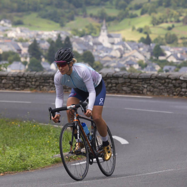 Une cycliste sur la route, village en arrière plan