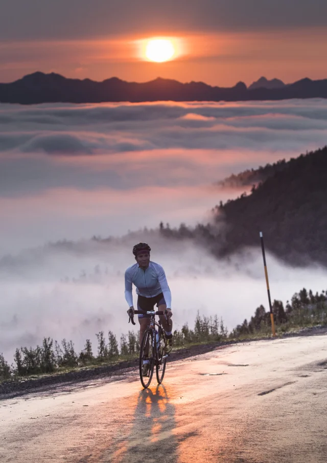 Une cycliste au sommet d'un col avec vue sur le coucher de soleil et les montagnes